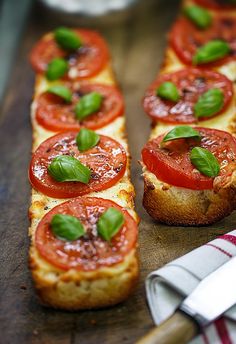 several slices of bread with tomatoes and basil on them, along with a knife to the side