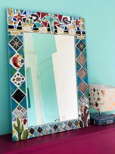 a mirror sitting on top of a purple dresser next to a lamp and a vase