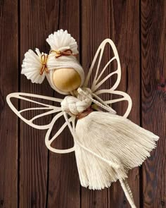 a white fairy doll made out of yarn and tassels on a wooden surface