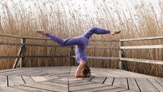 a woman is doing a handstand on a wooden deck in front of tall grass