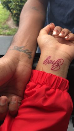 two people holding hands with tattoos on their wrist and the word love written in red ink