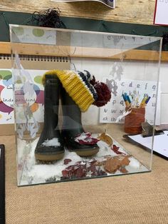 a pair of boots in a glass case with snow on the ground and other items behind it