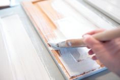 a person is painting on the wall with white paint and a wooden brush in their hand