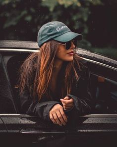 a woman in sunglasses and a hat leaning out the window of a car