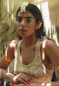 a woman with green eyes and gold jewelry on her head sitting in front of a wall