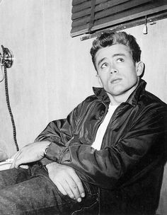 a black and white photo of a man sitting in front of a wall mounted telephone