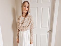 a woman standing in front of a white door wearing a sweater and skirt with heels