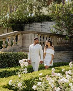 a man and woman dressed in white are walking through the garden with roses on the ground