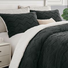 a bed with black and white comforter, pillows and blankets on top of it