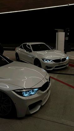 two white cars parked next to each other in front of a gas pump at night