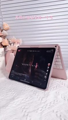 an open laptop computer sitting on top of a white bed next to a vase with flowers