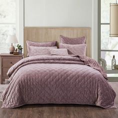 a bed with a purple comforter and pillows on top of it in a room