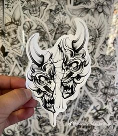 a hand holding up a sticker with an image of a demon head on it