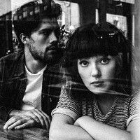 a man and woman sitting next to each other in front of a glass window with their arms crossed