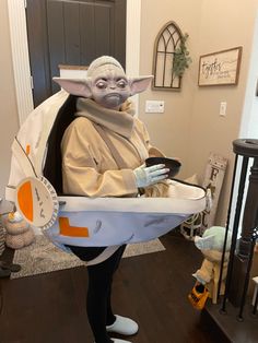 an adult yoda costume is shown in the living room, holding a tray with food on it