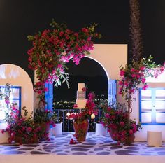 a wedding cake surrounded by potted flowers and candles on a table with lights in the background