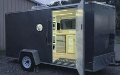 an enclosed trailer with its door open and the interior lit up at night, in front of a building