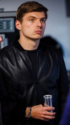 a man in a black leather jacket holding a drink and looking off into the distance