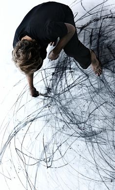 a man standing on top of a white floor covered in black and grey lines with his head down