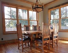 a dining room table and chairs in front of two large windows with wood flooring