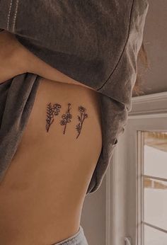 a woman's back with three small tattoos on her left side, and flowers in the middle