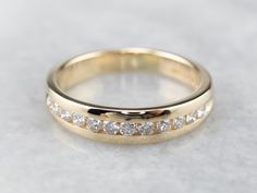 a yellow gold wedding ring with five diamonds on it's side, sitting on a white surface