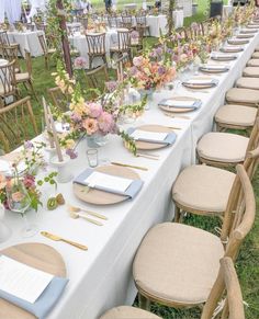 a long table set up with place settings and flowers on it for an outdoor event