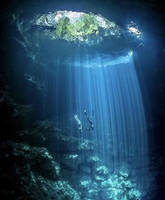 two people are swimming in the water near a large hole that looks like an underwater cave