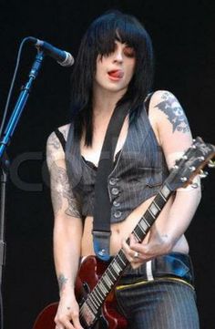 a woman with black hair and piercings playing an electric guitar in front of a microphone