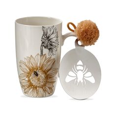 a mug with a bee and sunflower on it next to a pom - pom