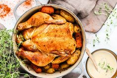 a roasted chicken in a pot with carrots and potatoes next to a glass of ranch dressing