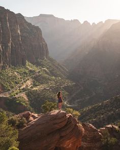 a woman standing on the edge of a cliff looking out over a valley and mountains