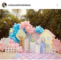 a table topped with pink and blue balloons next to a white fence covered in animals