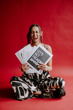 a woman sitting on the floor holding up some papers and smiling at the camera while wearing zebra print pants