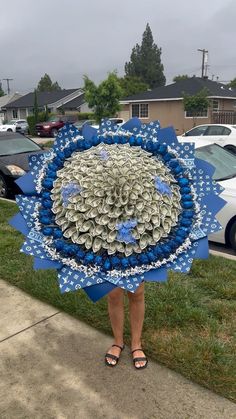 a woman is standing on the sidewalk holding a blue and white paper art piece in front of her