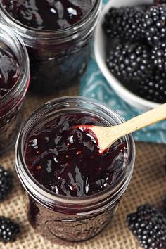 several jars filled with jam on top of a table next to bowls of blackberries