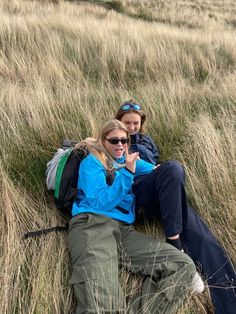 two women laying on the ground in tall grass with their backpacks over their shoulders