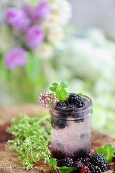 a jar filled with lots of blackberries next to green leaves and berries on a table