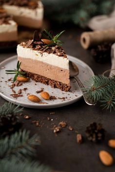 a piece of cake on a plate with nuts and greenery next to it, surrounded by other desserts