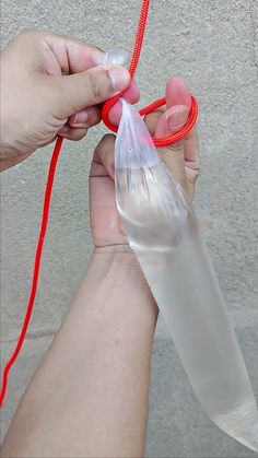 two hands holding an object with red string and plastic bag attached to it, while another person holds the item in their hand