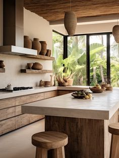 a kitchen with an island counter and stools in front of the window that looks out onto the jungle