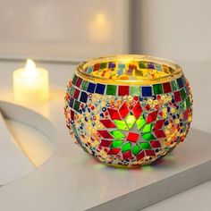 a colorful mosaic glass candle holder sitting on top of a counter next to a lit candle