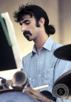 a man with a moustache on his face sitting in front of a motorcycle