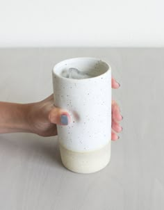 a hand holding a white cup on top of a table