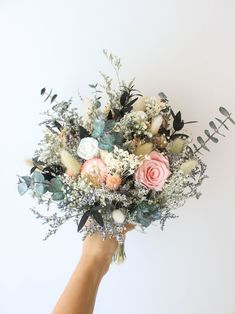 a hand holding a bouquet of flowers against a white wall with greenery on it