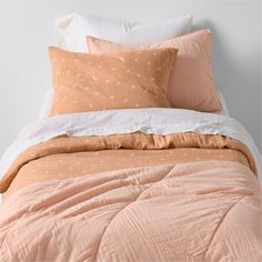 an orange and white comforter on top of a bed next to two pillow cases