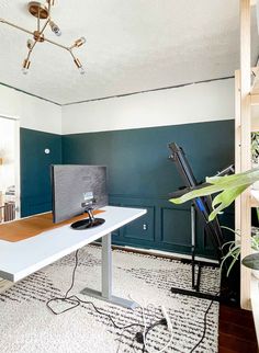 a room with a desk, chair and computer monitor on it in front of a blue wall