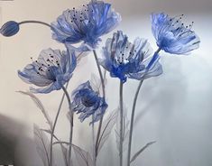 some blue flowers are in front of a white wall with black dots on it and the stems appear to be wilting