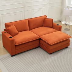 an orange couch with two pillows on it in front of a white wall and floor