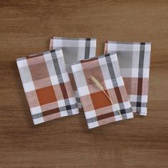 three plaid napkins with a feather on them sitting on top of a wooden table